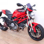 Ducati Monster 2011 - Moto Ducati Monster roja con chasis tubular, escape lateral doble y vista diagonal del lado izquierdo.